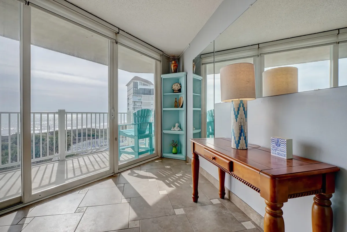 A tranquil corner with a blue accent chair and a wooden console table, bathed in natural light from expansive windows that frame a stunning ocean panorama. Ideal for quiet moments, small gatherings, or simply admiring the view.