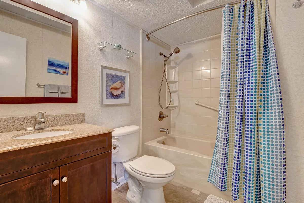 An inviting bathroom with a vanity, sink, bathtub, shower curtain, and mirror. The serene mood and thoughtful layout suggest a space designed for relaxation, whether indulging in a soothing soak or refreshing shower after a day at the beach.