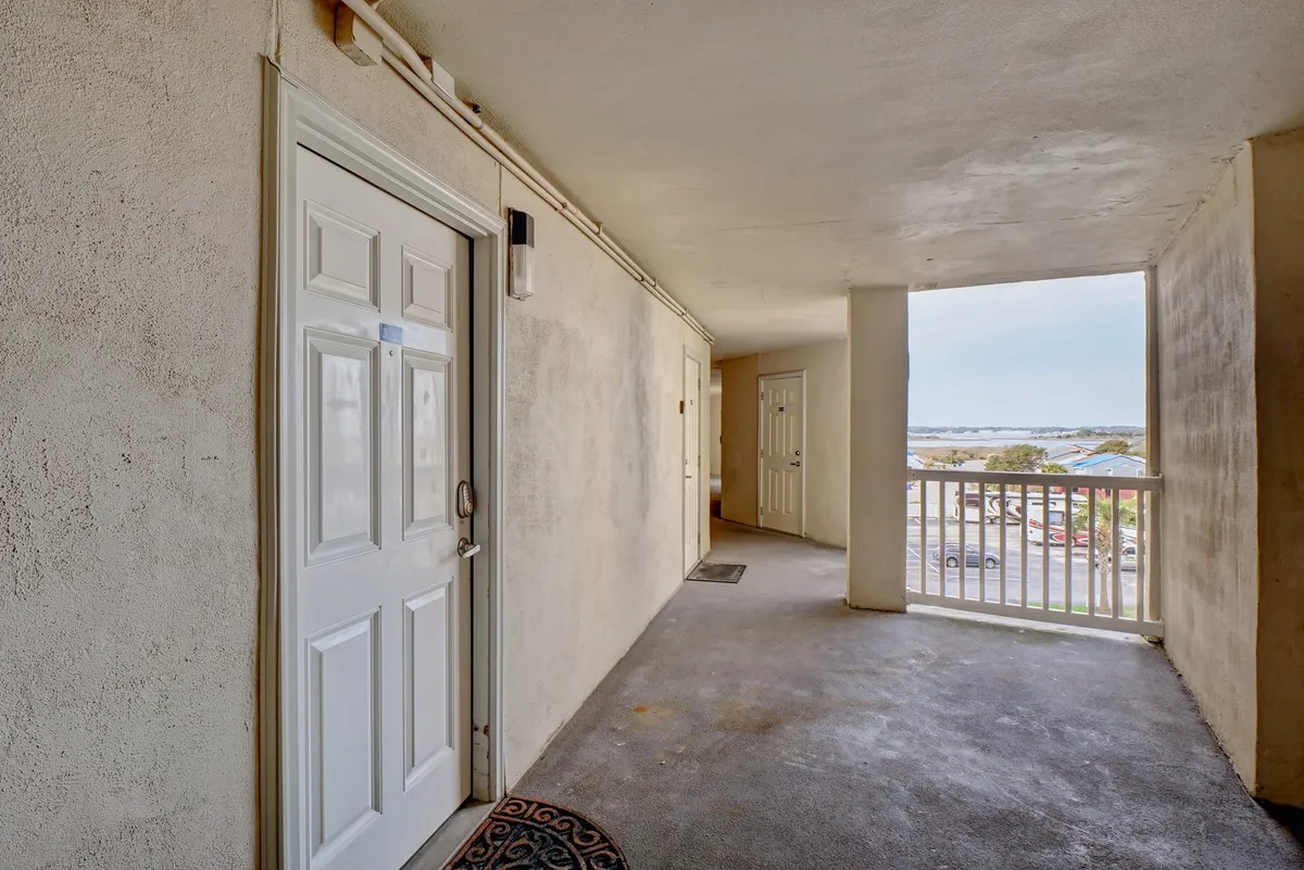 Captured from an interior vantage, this image frames the front and side doors leading out to a private balcony. The view from the balcony hints at the ocean horizon and sunset skies, suggesting a place to unwind and enjoy tranquil evenings.