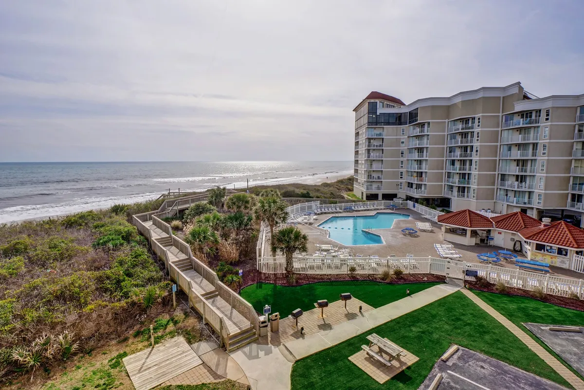 A spacious outdoor swimming pool surrounded by landscaped grounds, with the ocean visible in the background. Lounging areas invite guests to relax and soak up the sun.