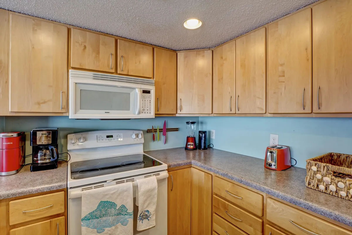 A modern, fully equipped kitchen with stainless steel appliances and light wood cabinetry. Subtle personal touches like a colorful dish towel add warmth, inviting guests to imagine cooking or baking together.