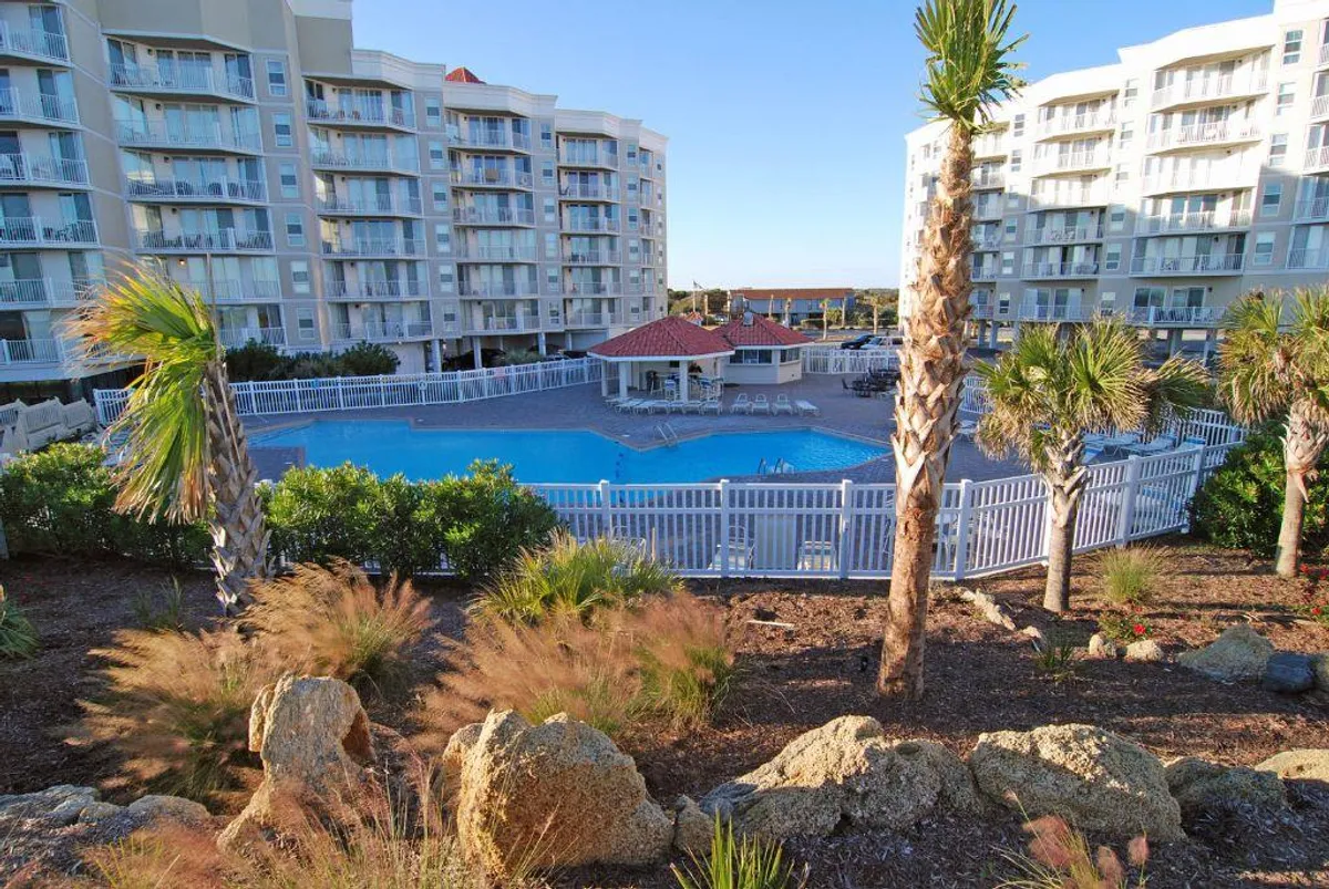 A lively scene focused on the swimming pool area, surrounded by palm trees, lounge chairs, and hints of the residential buildings. The lighting suggests late afternoon, highlighting the inviting warmth and leisure of the poolside environment.